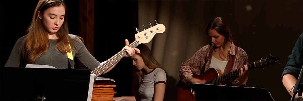 students performing music on stage, woman in foreground playing electric bass